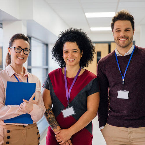 Three teachers or staff members standing in a hallway wearing badges