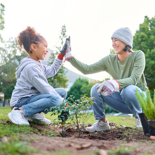 A woman and young girl squatting in a garden giving each other a high five